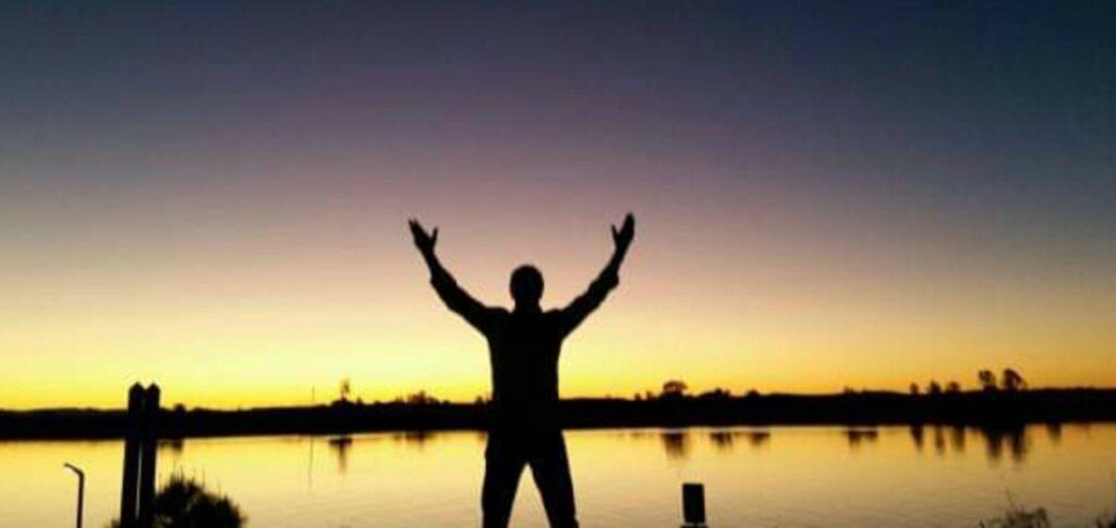 Person with hands up in air at edge of water